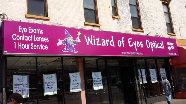 Storefront sign for “Wizard of Eyes Opticians” with eye exams, contact lenses, and 1-hour services.