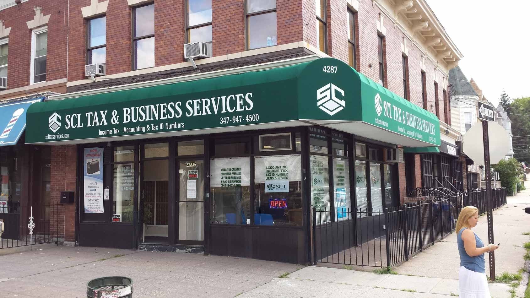Corner storefront with green awning for a tax and business services office, with sidewalk seating outside