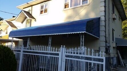 Two-story house with blue awning and white fence in front of a gated porch