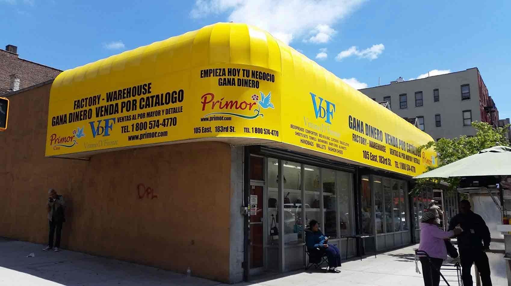 Corner storefront with bright yellow awning, glass windows, and a few people walking by on a sunny street.