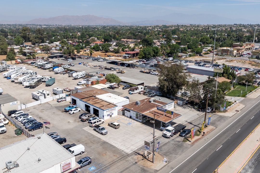 Aerial view of a truck yard with parked vehicles, small buildings, and a road beside a desert town.