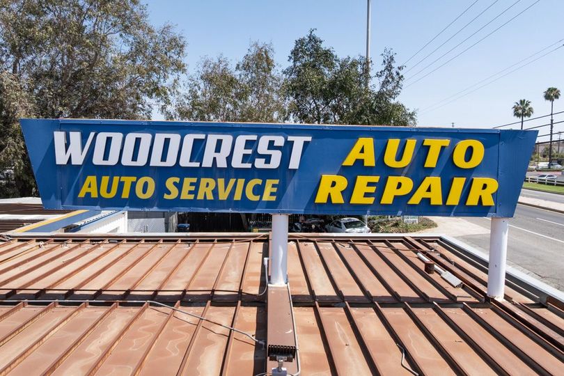 Blue and yellow Woodcrest Auto Service and Auto Repair rooftop sign against trees and sky