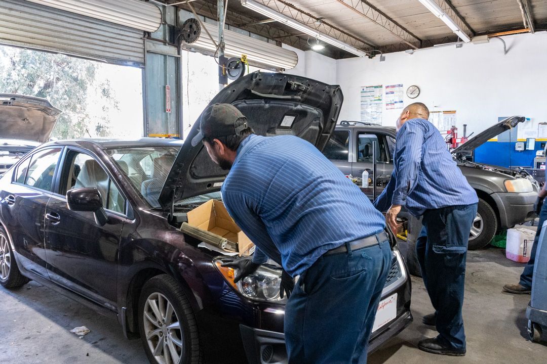 Mechanics working under the hood of a black car in an auto repair shop