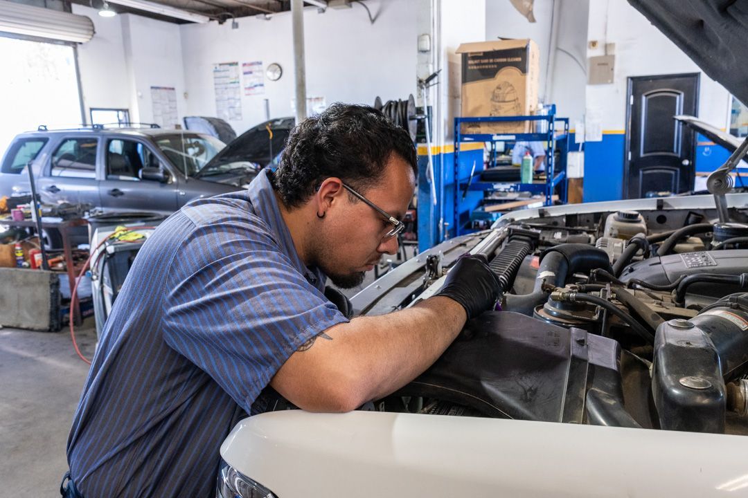 Mechanic inspecting a car engine in an auto repair shop, with blue equipment and another car in the background