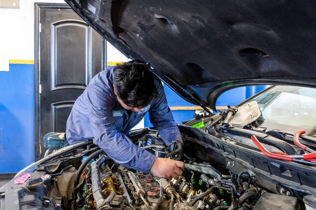 Mechanic in blue coveralls working under a car hood in an auto shop