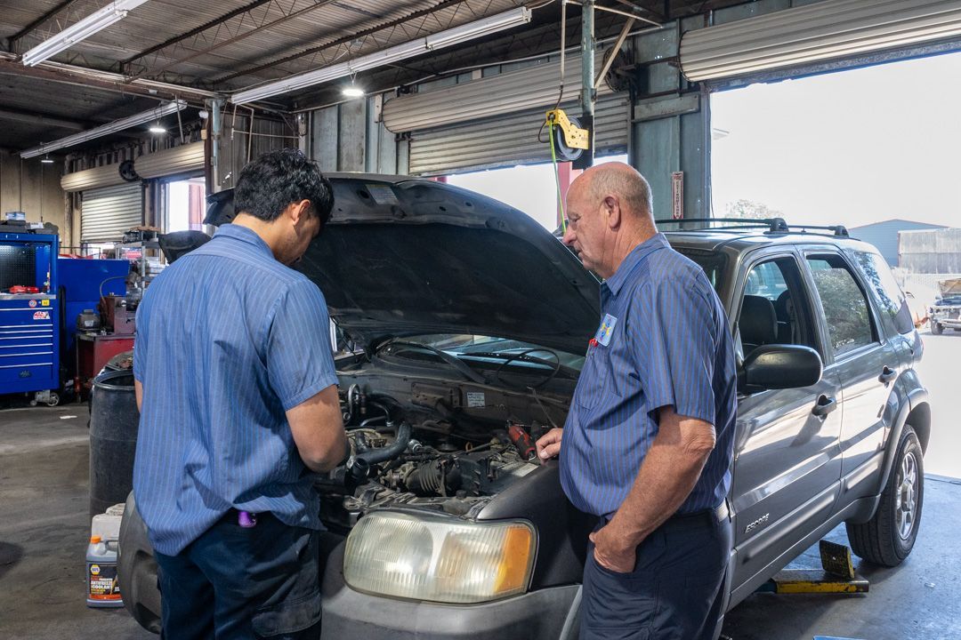 Two mechanics inspecting a black SUV with its hood open in a garage