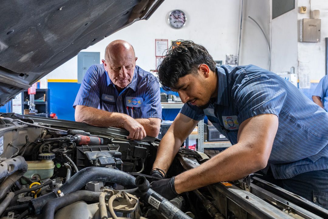 Two mechanics working under a car hood in a garage, inspecting the engine.