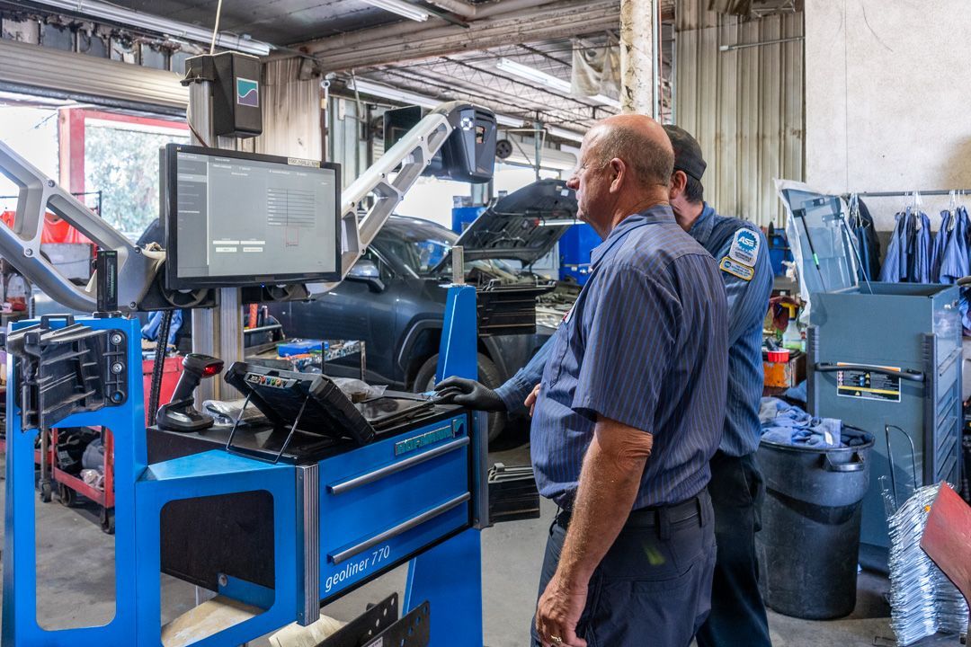 Worker in a blue industrial workshop inspecting equipment at a monitor beside a machine.