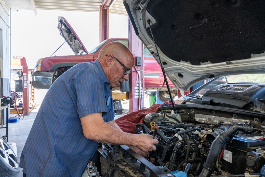 Mechanic working on a car engine with the hood open in an auto repair shop