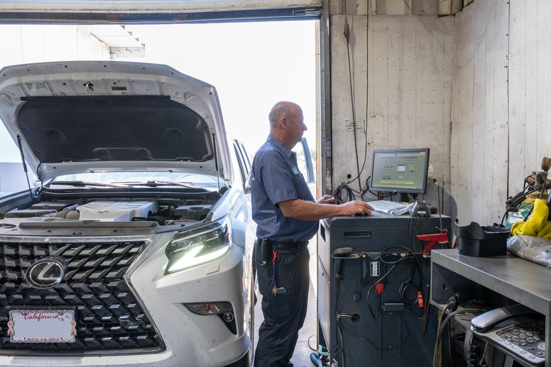 Mechanic working at a laptop beside a white SUV with its hood open in a garage