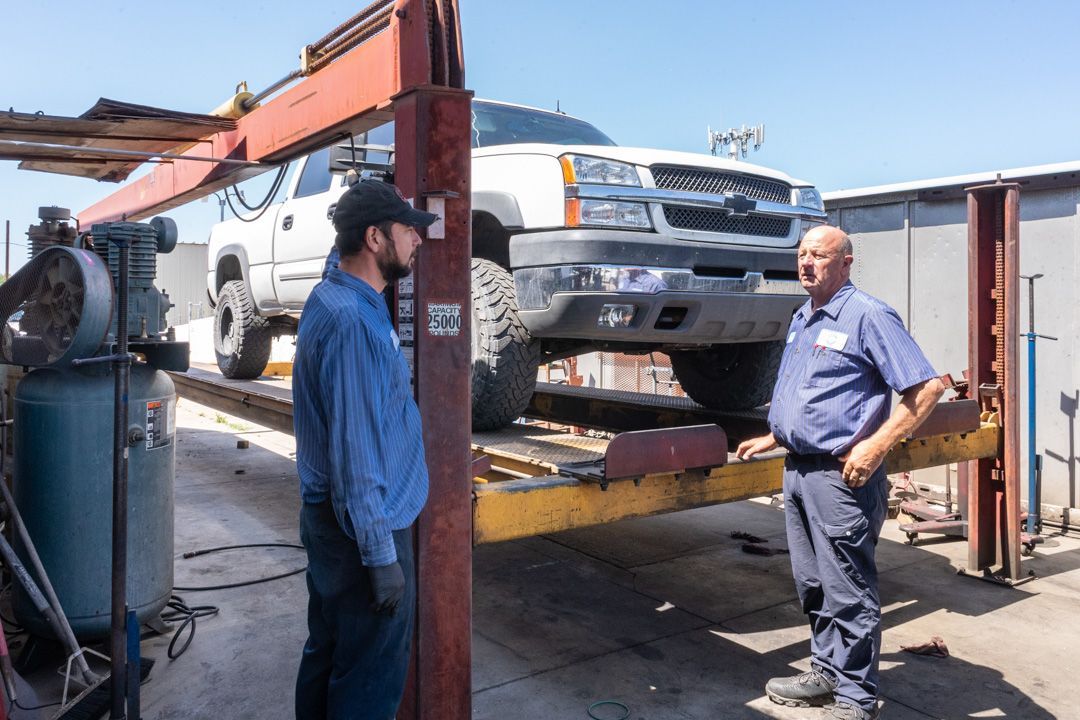 Pickup truck on a lift at an auto shop, with two men standing beside it