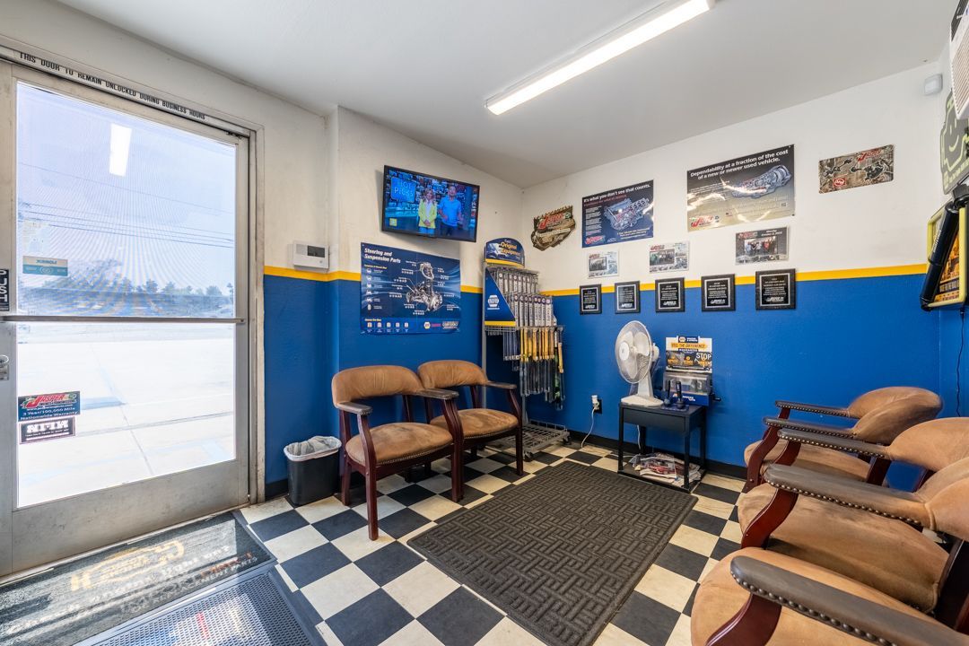 Barbershop waiting area with blue walls, checkered floor, chairs, TV, and barber tools