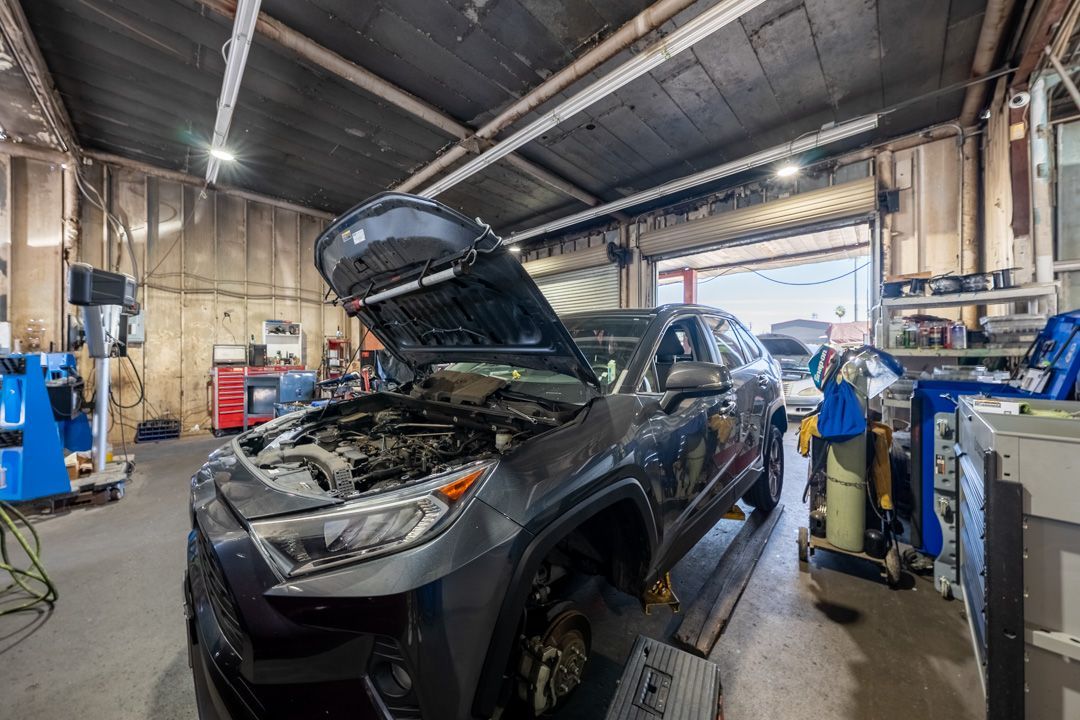 Black car with hood open in an auto repair shop beside a mechanic and equipment