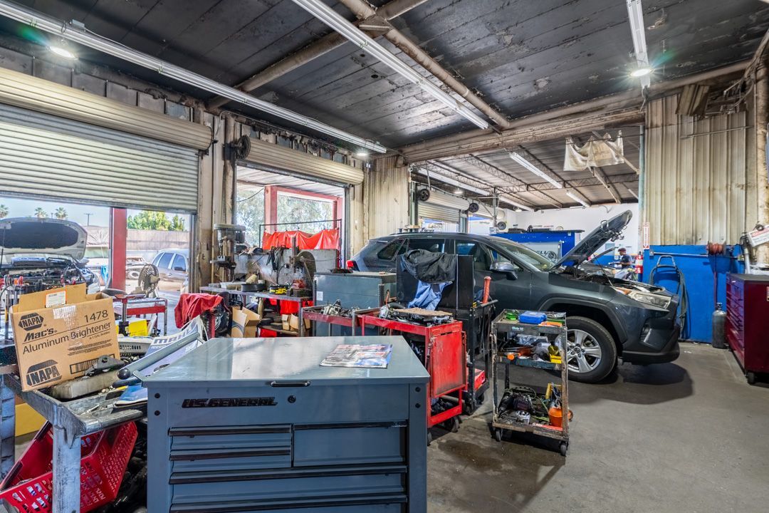 Automotive repair garage with a black car, red tools, and boxes under bright overhead lights