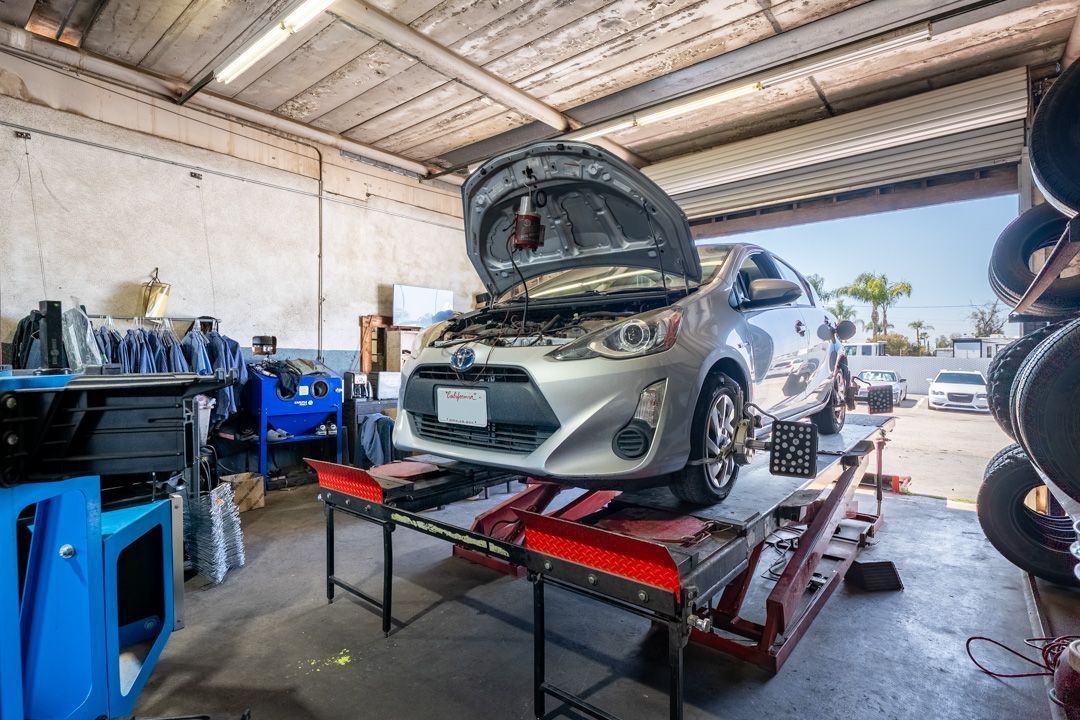 Silver car on a lift in an auto repair garage with its hood open and tools nearby