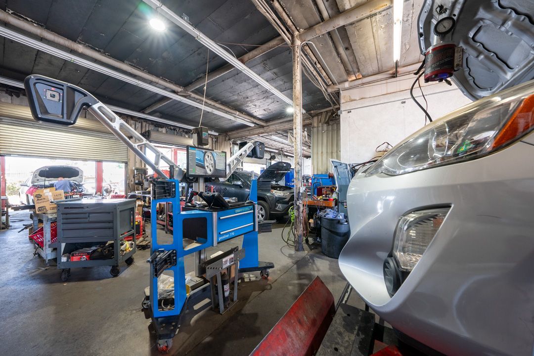 Car repair shop interior with raised silver car, blue lift equipment, and mechanics working under bright lights
