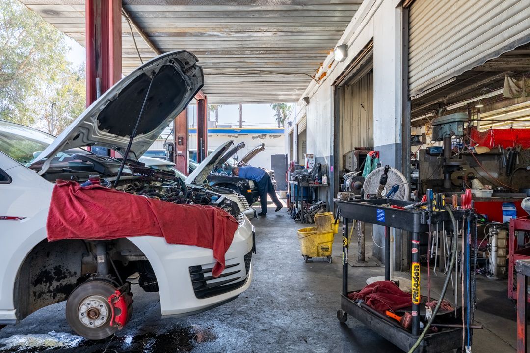 Auto repair shop with a white car on a lift, hood open, and tools and bike parts along the bay