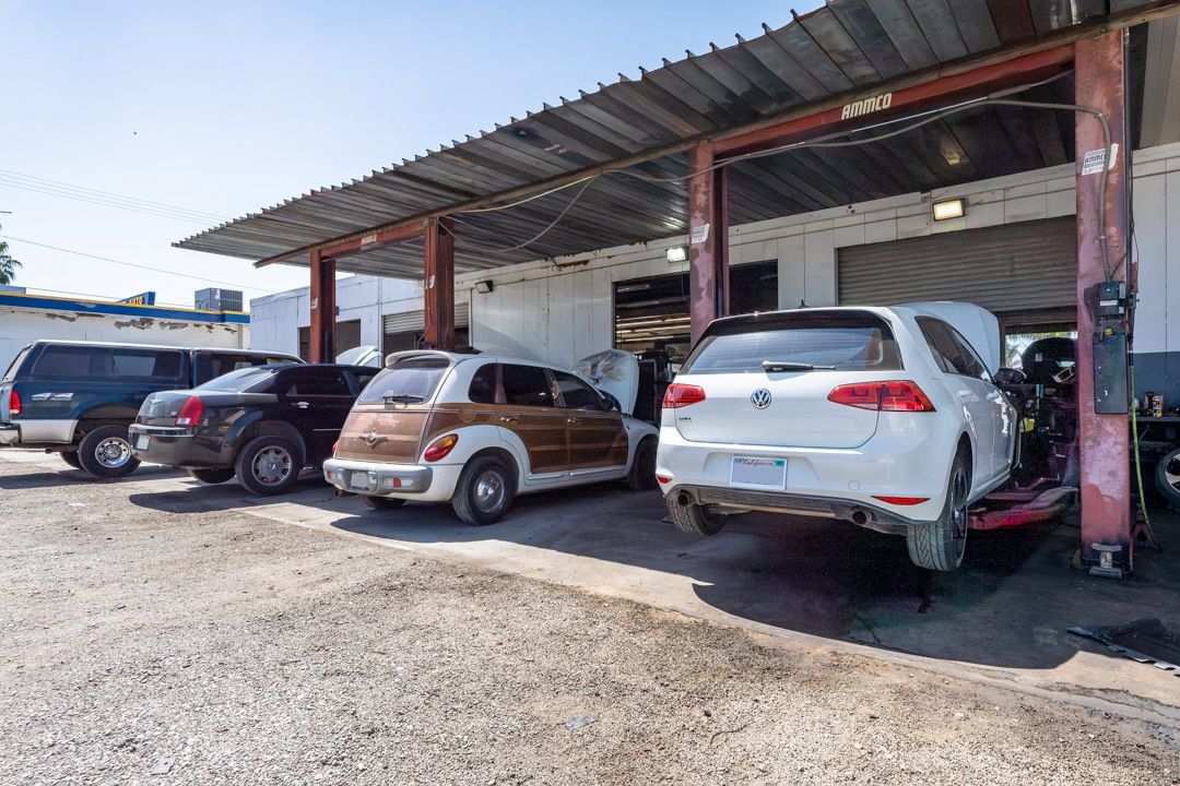 Three parked cars under a metal-roofed carport, including a white SUV and a brown compact car.