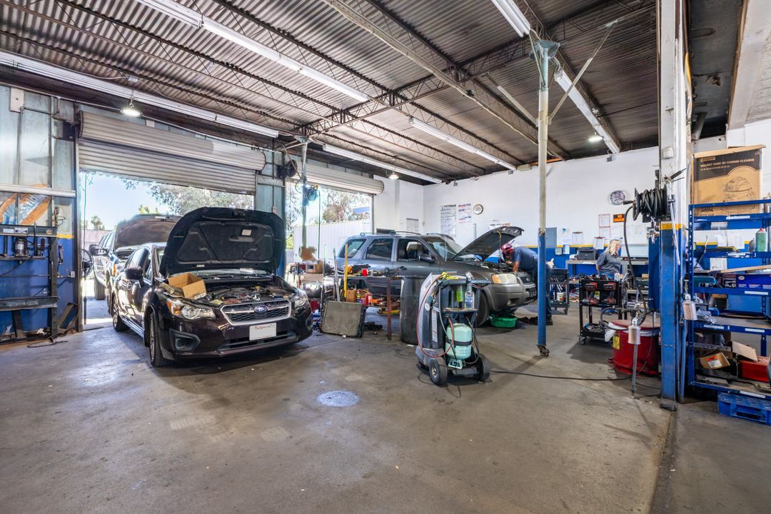Auto repair shop with several cars, one with hood open, and blue tool racks inside a garage