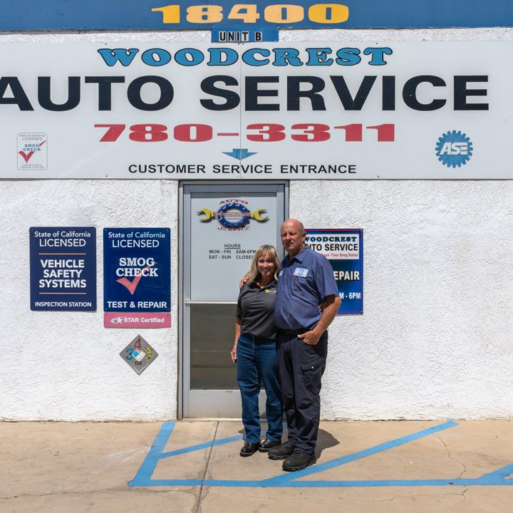 Two people standing outside a Woodcrest Auto Service storefront with large signage and blue curb markings