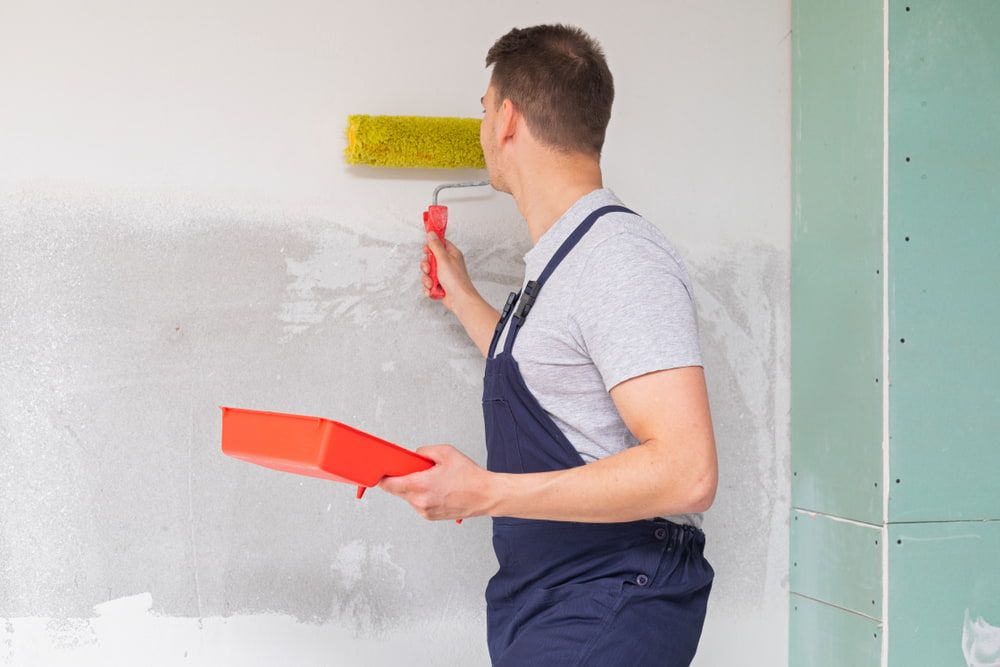 A Man Is Painting A Wall With A Paint Roller — Ballina Painting Service In Evans Head, NSW