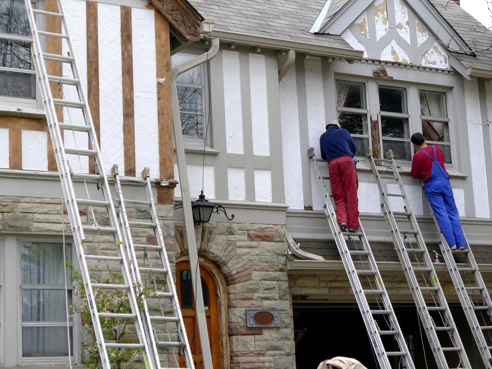 Two Men Are Painting The Side Of A House With Ladders — Ballina Painting Service In Lismore, NSW