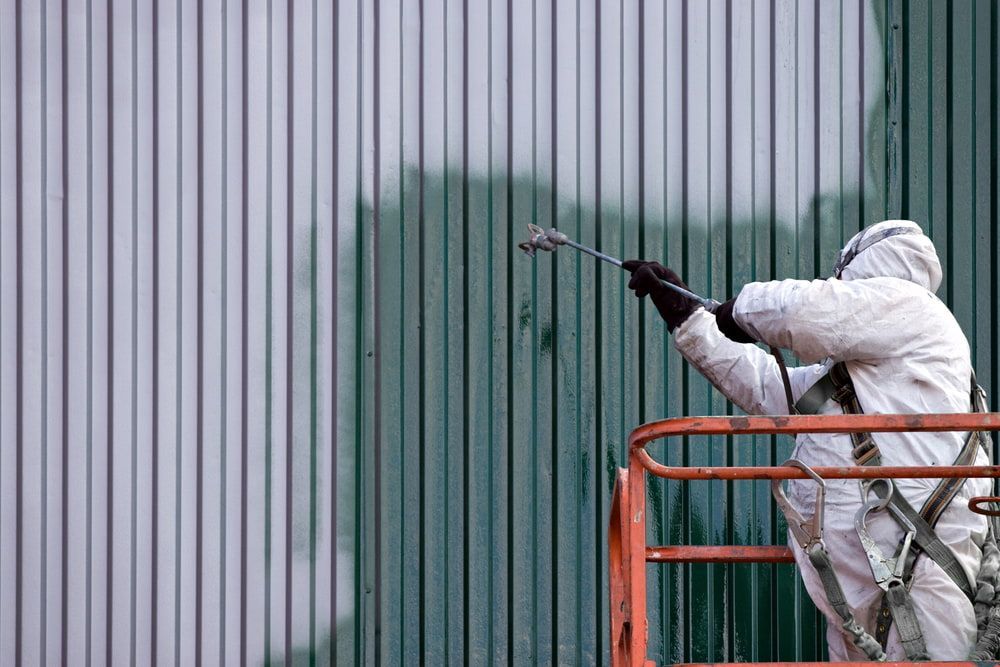 A Man In A Protective Suit Is Painting A Wall On A Lift — Ballina Painting Service In Lismore, NSW