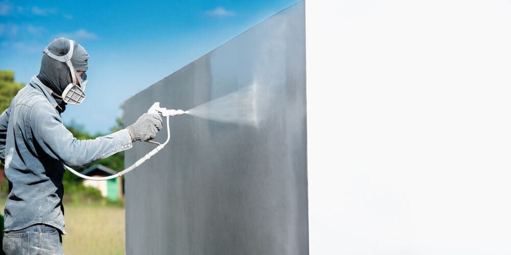 A Man Wearing A Mask Is Spraying Paint On A Wall — Ballina Painting Service In Ballina, NSW