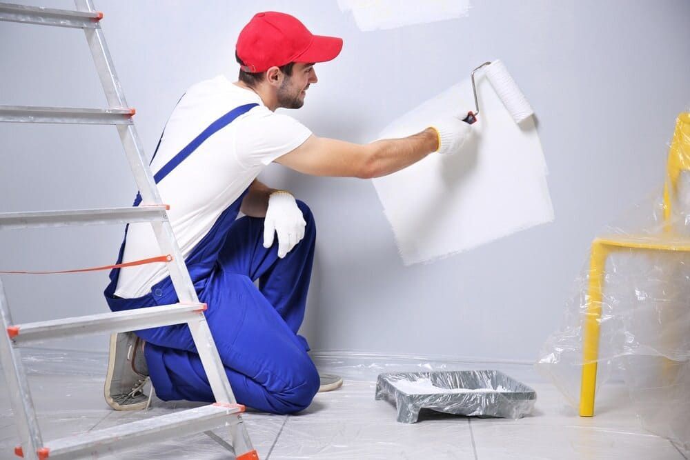 A Man Is Kneeling Down While Painting A Wall With A Roller — Ballina Painting Service In Brunswick Heads, NSW