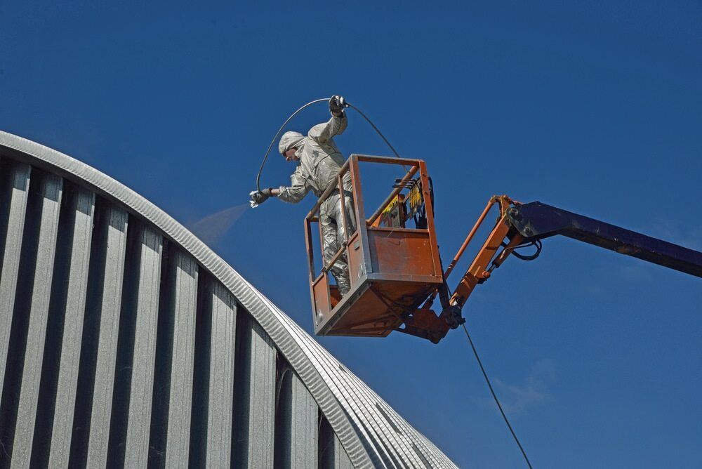 A Man Is Spraying Paint On The Side Of A Building — Ballina Painting Service In Lismore, NSW