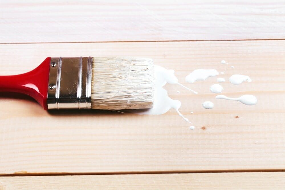 A Paint Brush With White Paint Spilling Out Of It On A Wooden Surface — Ballina Painting Service In Brunswick Heads, NSW