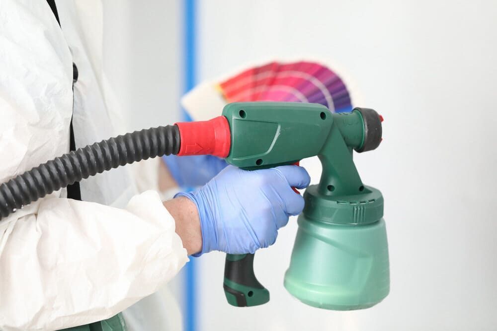 A Man Wearing Gloves Holds A Paint Sprayer With A Color Palette — Ballina Painting Service In Alstonville, NSW