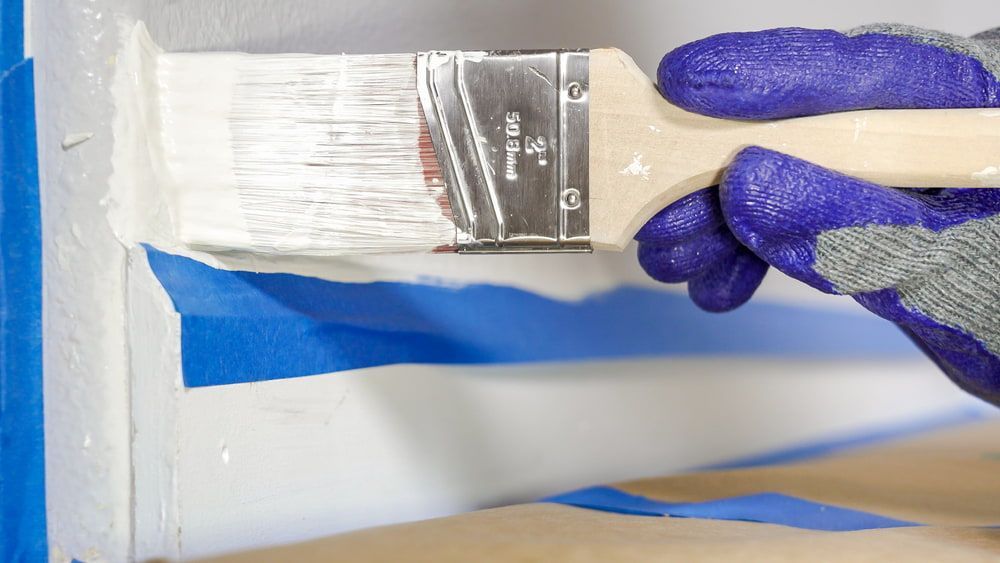 A Person Is Holding A Paint Brush With White Paint On It — Ballina Painting Service In Lennox Head, NSW