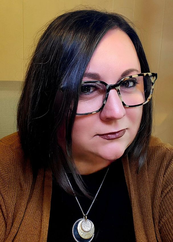 A woman wearing glasses and a necklace is looking at the camera.