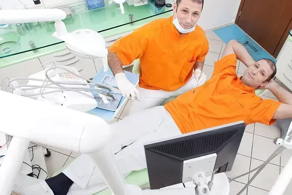Un dentista visita un paziente sdraiato, con un altro assistente nelle vicinanze, in una luminosa clinica odontoiatrica.