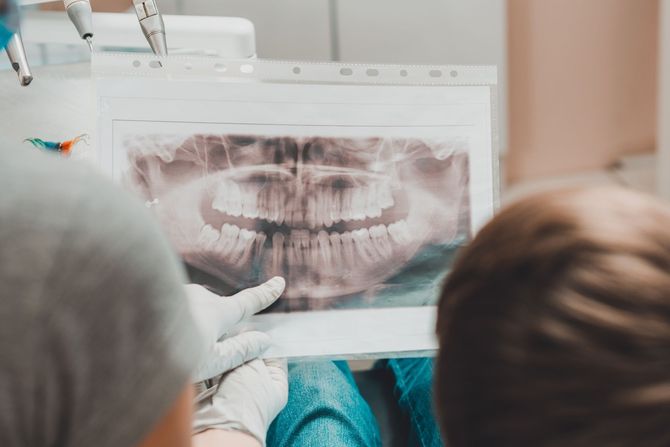 Un dentista mostra una radiografia panoramica dei denti a due pazienti seduti in una clinica.