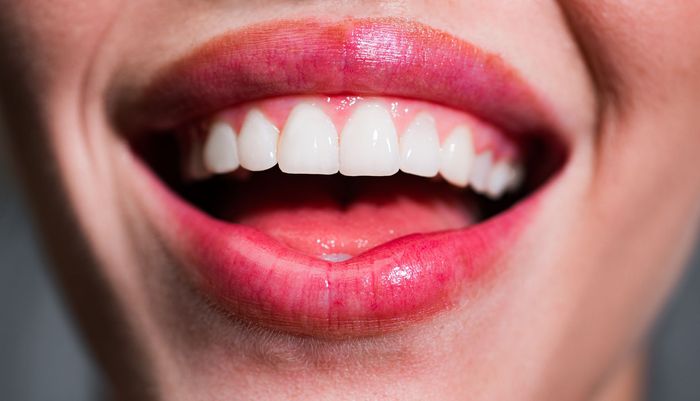 Primo piano di una bocca sorridente con rossetto rosa lucido e denti bianchi