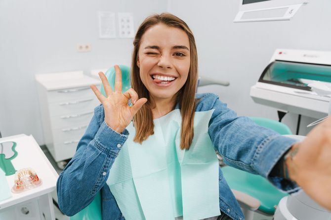 Una paziente sorridente con un bavaglino color menta fa il segno 