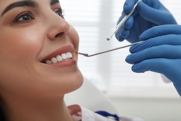 Una donna sorride mentre un dentista le sistema l'apparecchio con le mani guantate.