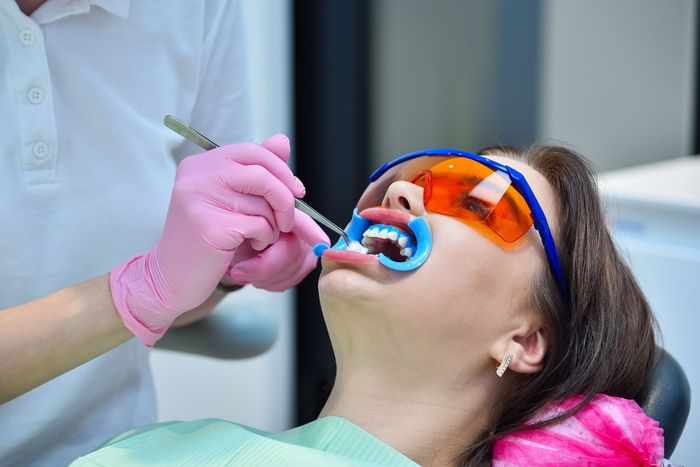 Un dentista con guanti rosa esamina i denti di un paziente con uno specchietto dentale e occhiali di sicurezza arancioni.