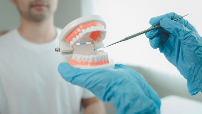 Un dentista, indossando guanti blu, dimostra l'importanza delle cure dentistiche su una bocca artificiale utilizzando uno strumento.