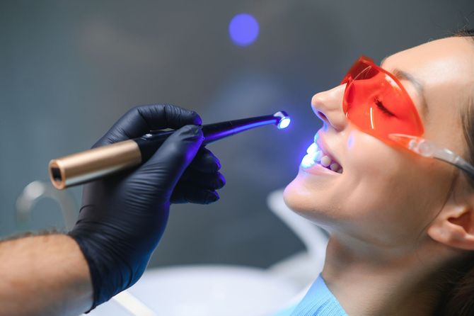 Dentista che utilizza una lampada polimerizzatrice blu su un paziente che indossa occhiali protettivi rossi.