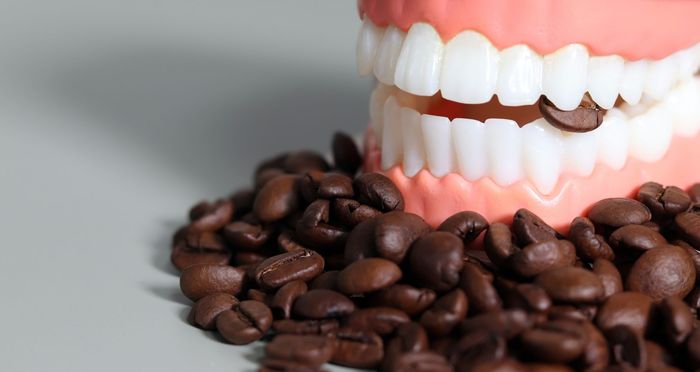 Primo piano di una bocca giocattolo sorridente accanto a una pila di chicchi di caffè.