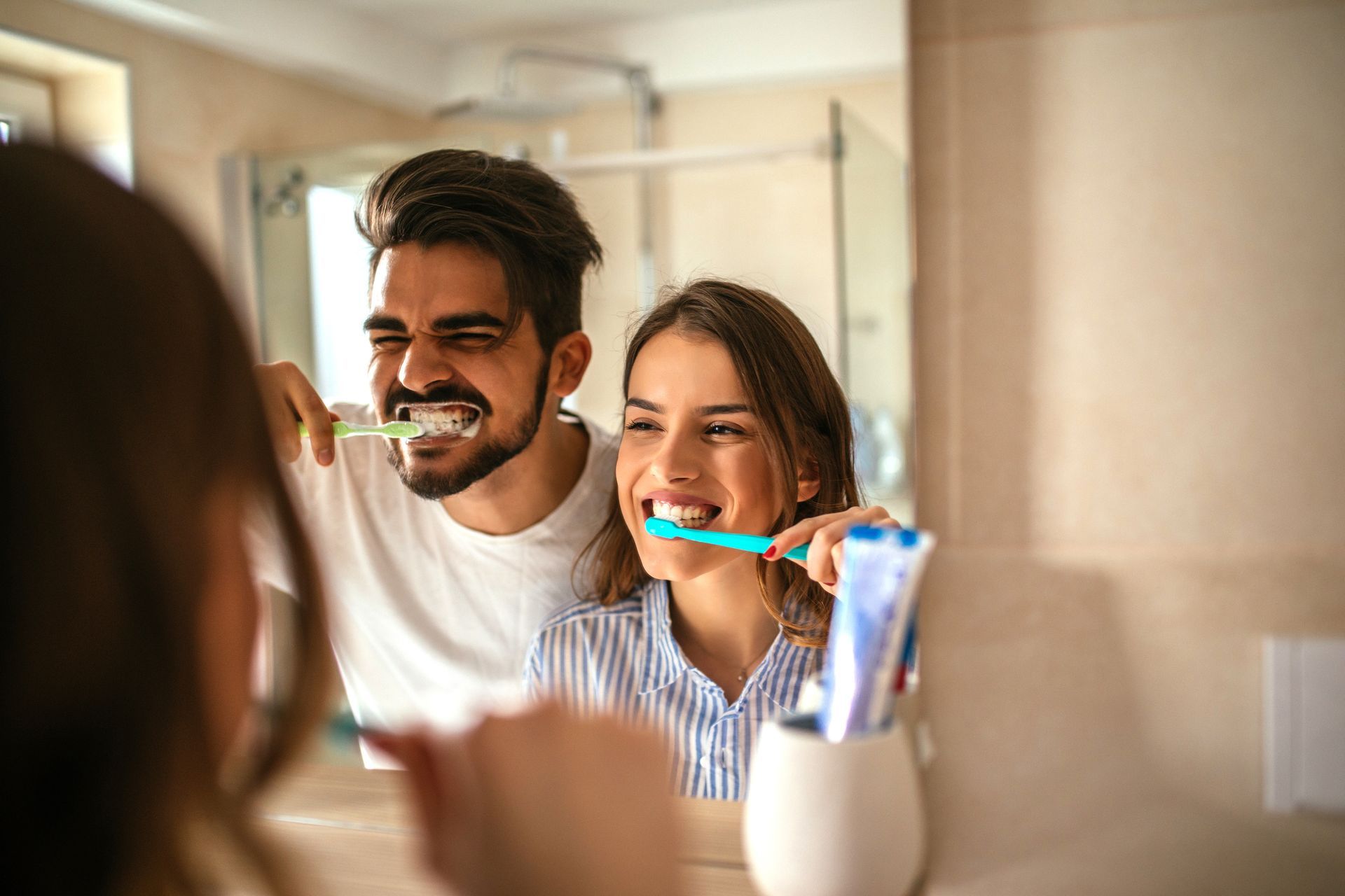 Due persone che si lavano i denti davanti allo specchio del bagno, sorridendo insieme.