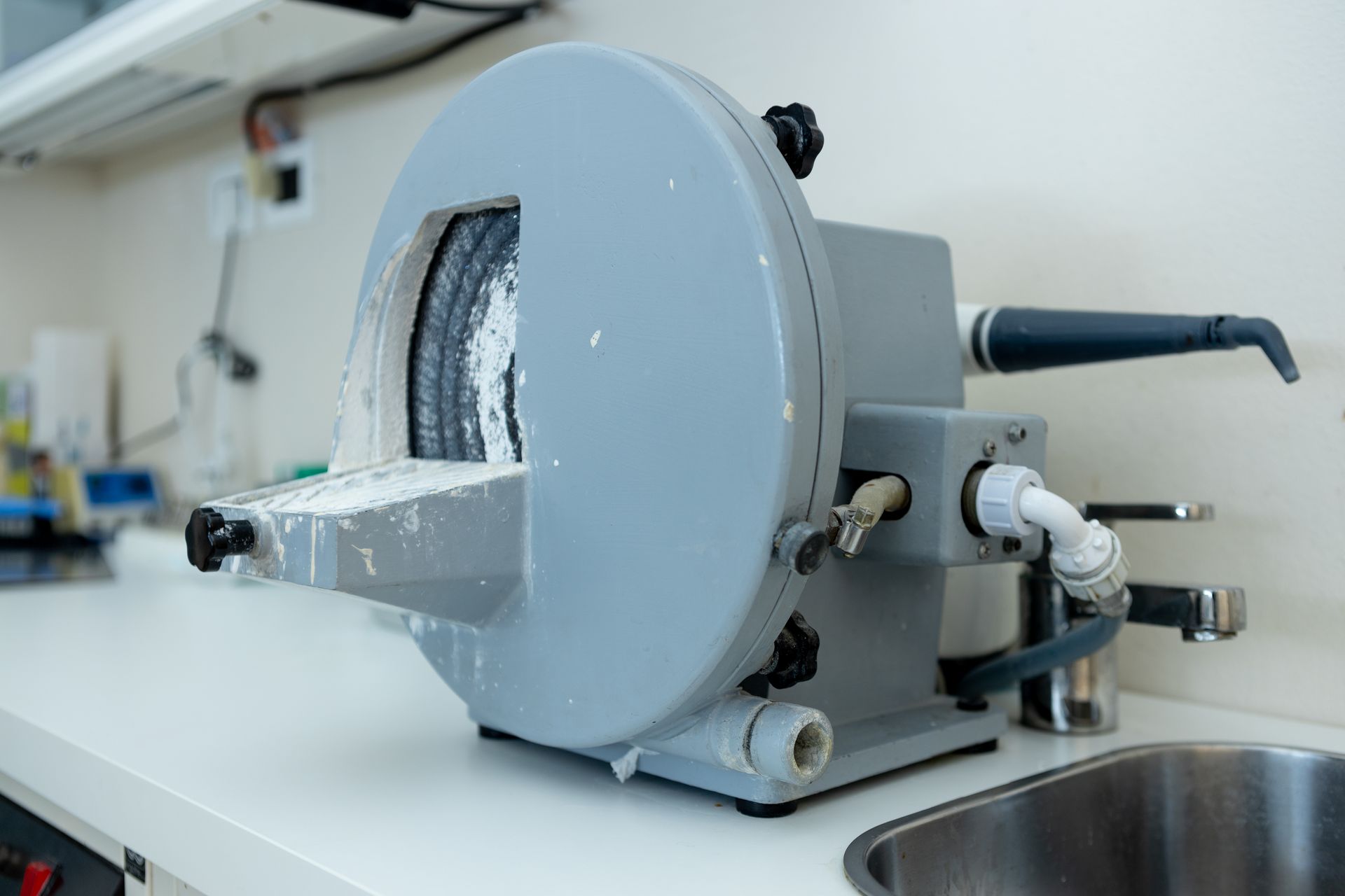 Macchina industriale grigia con apertura frontale circolare su un piano di lavoro bianco in un laboratorio o in un'officina