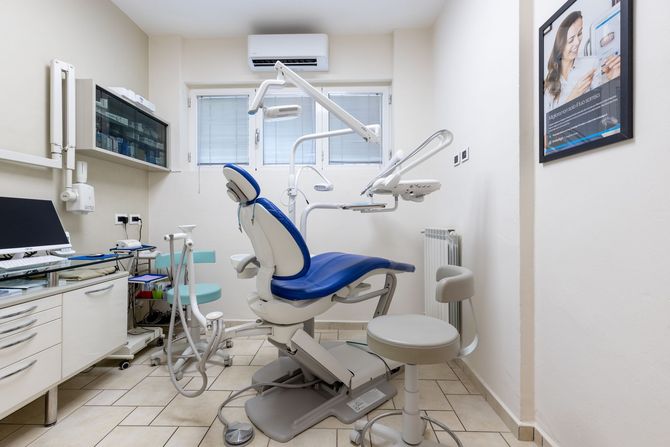 Moderna sala per visite odontoiatriche con poltrona blu, attrezzature, armadietti e monitor a raggi X.