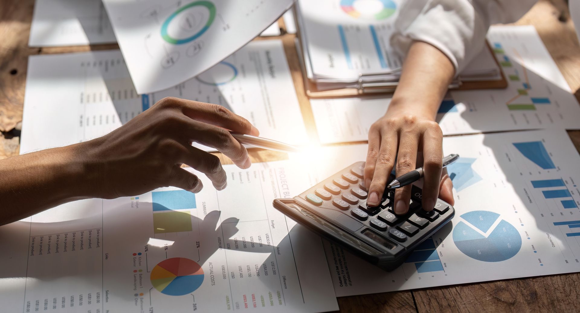 Two people calculating finances with charts and a calculator on a wooden table.