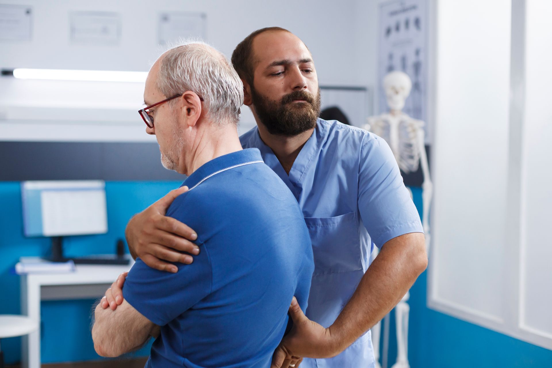 A chiropractor performing a spinal adjustment on an older male patient in a clinical exam room