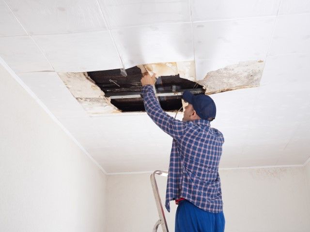 Person inspecting a water-damaged ceiling panel with an open hatch and stains