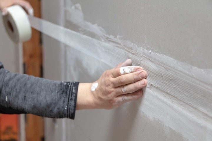 Hand smoothing white tape on a wall with a tape roll in the background